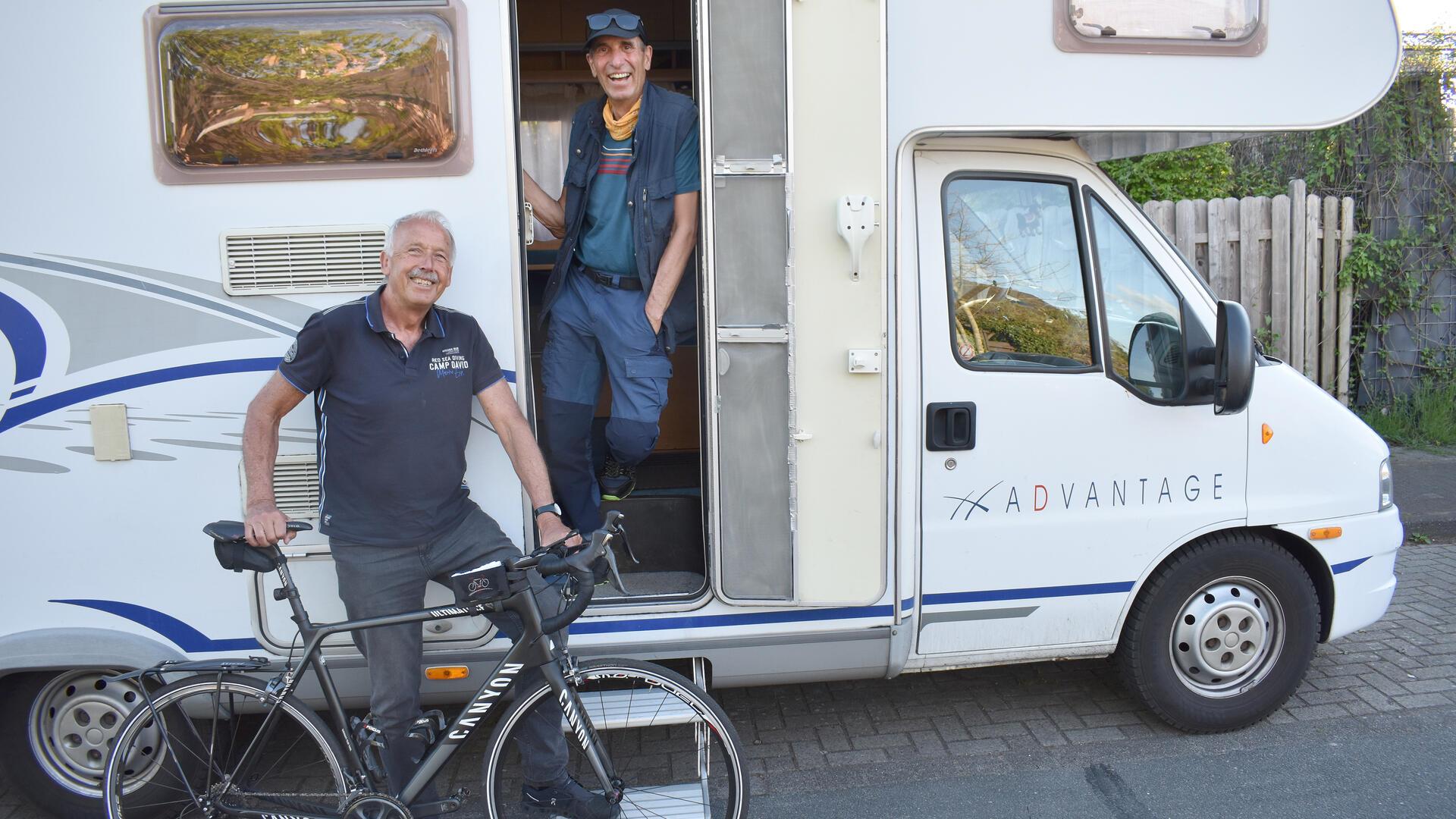 Zwei Männer, einer mit einem Fahrrad, stehen an einem Wohnmobil.