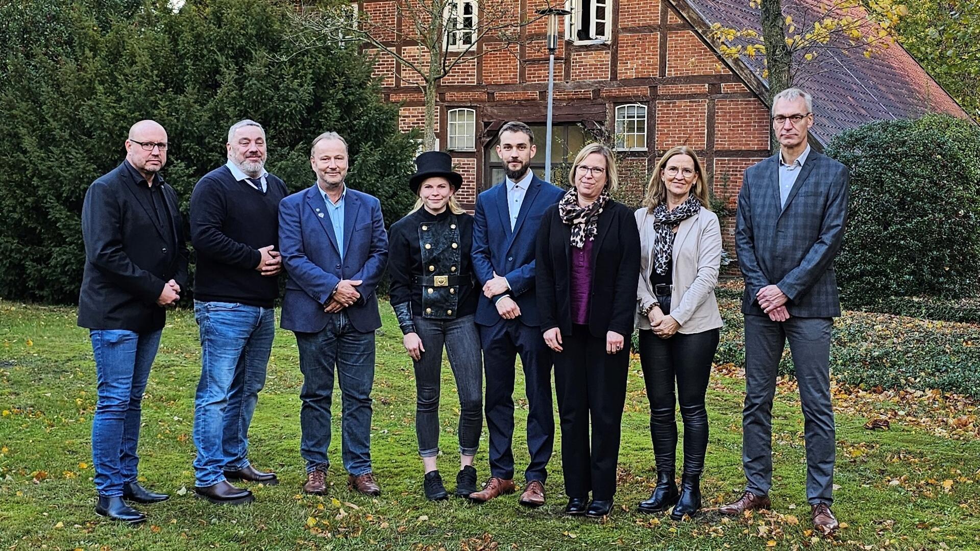 Gruppe von Menschen in Garten vor Fachwerkhaus; in der Mitte eine Schornsteinfegerin