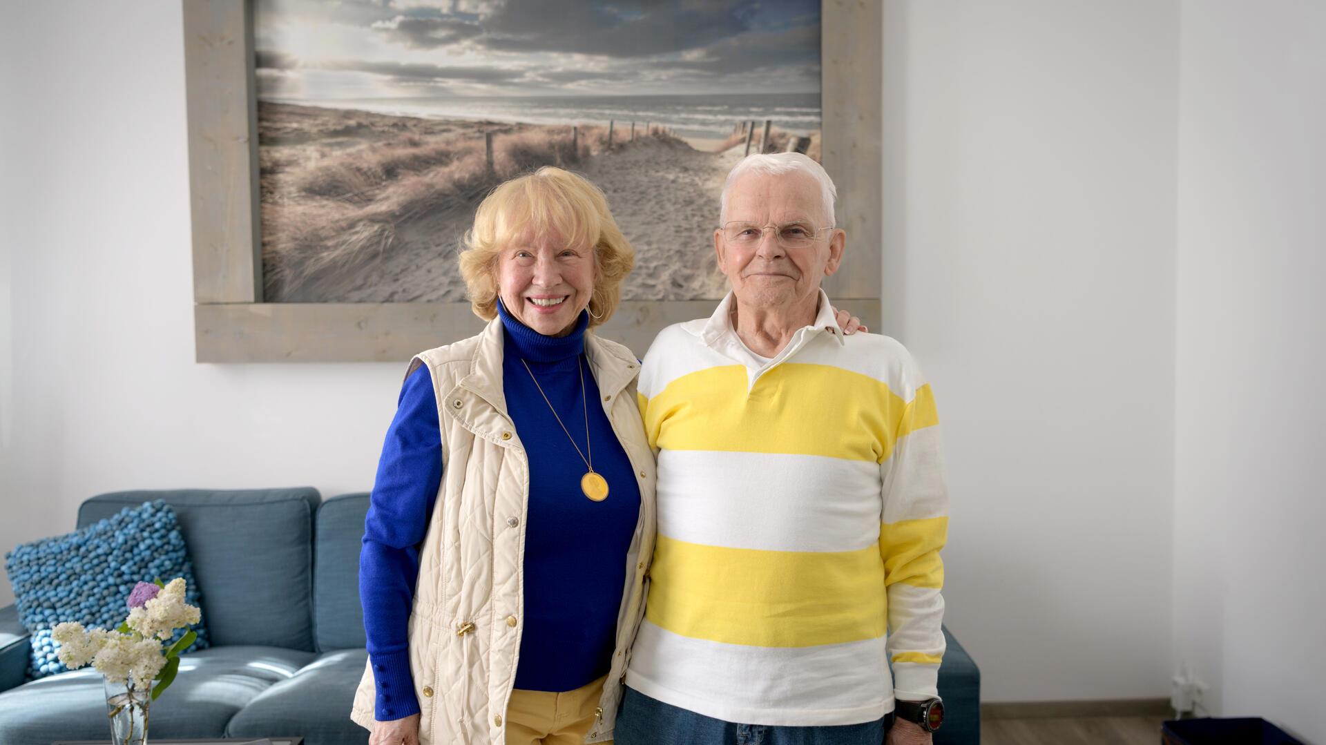 Eine Frau und ein Mann stehen in einem Wohnzimmer vor einem Bild, welches Strand und Meer zeigt.