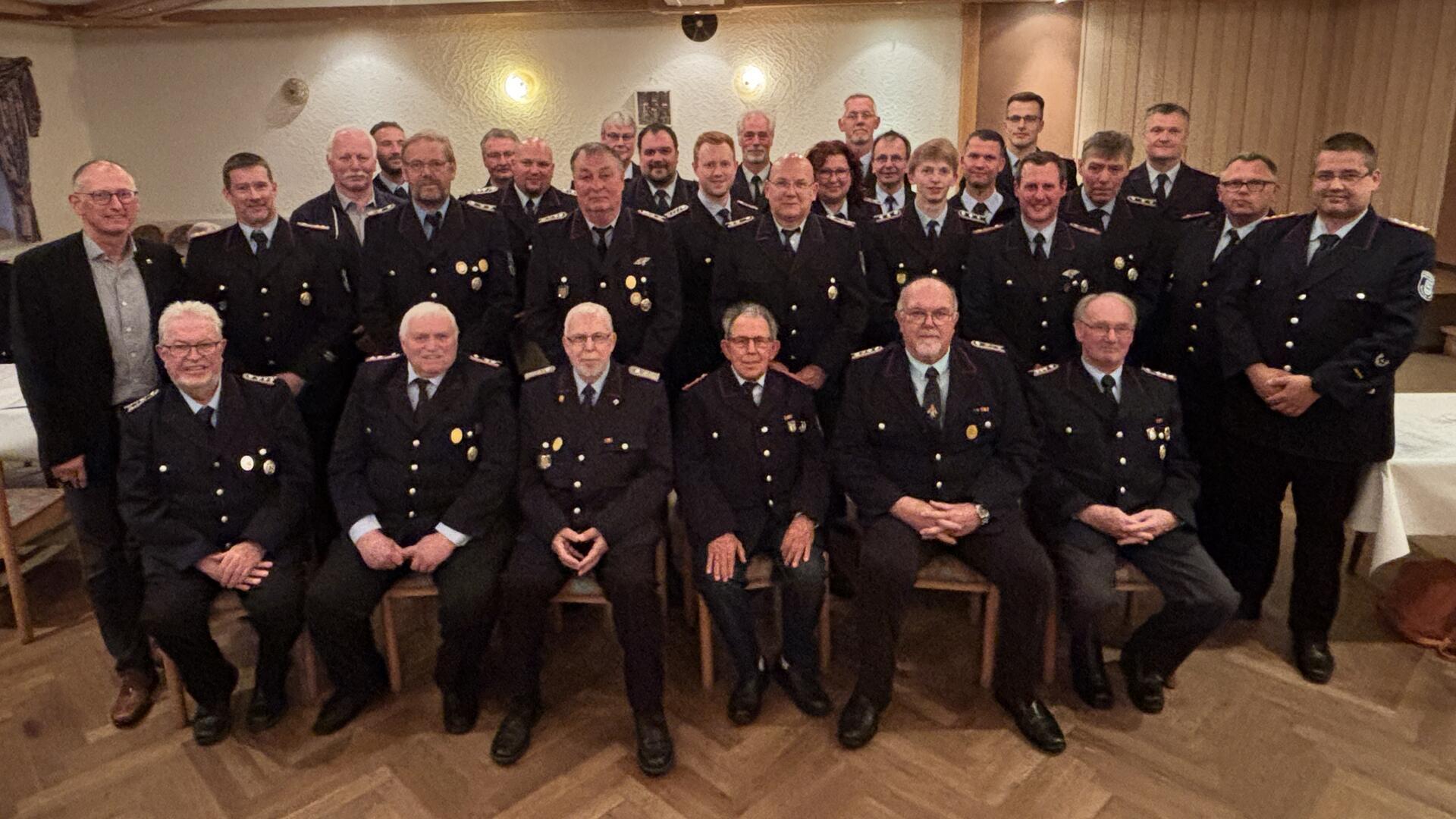 Gruppenbild von Feuerwehrkameraden der Freiwilligen Feuerwehr Loxstedt in Uniform, aufgenommen bei der Ehrungsveranstaltung in einem festlich dekorierten Saal. In mehreren Reihen sitzen und stehen die geehrten Mitglieder sowie Führungskräfte.