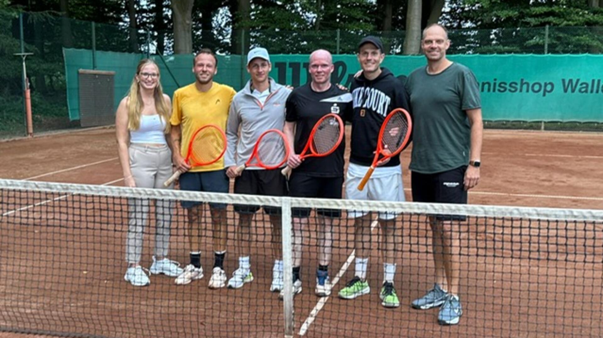 Mehrere Personen stehen auf einem Tennisplatz und halten Tennisschläger in den Händen.