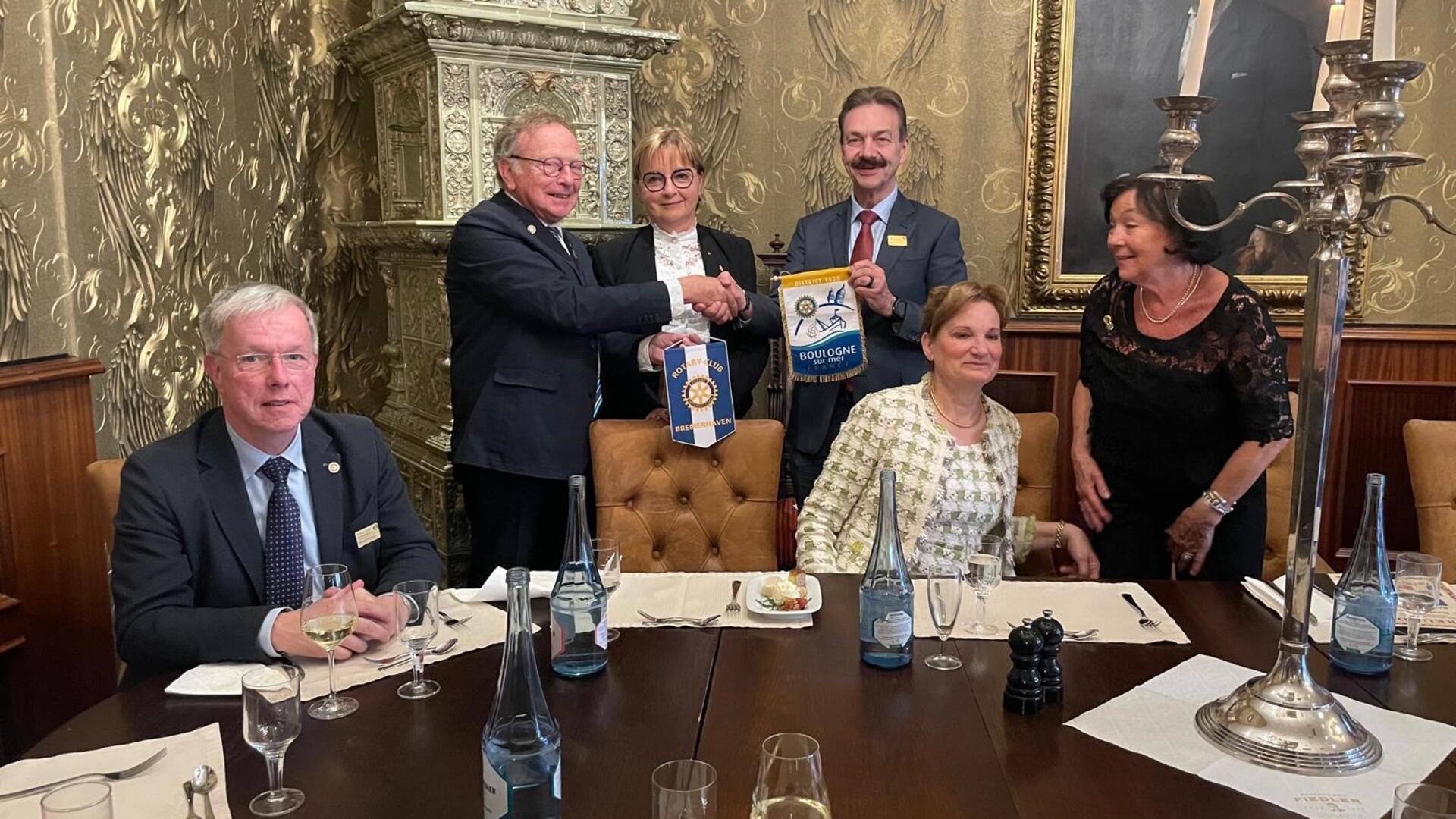 Männer und Frauen in einem Raum. Zwei Männer tauschen Geschenke aus.