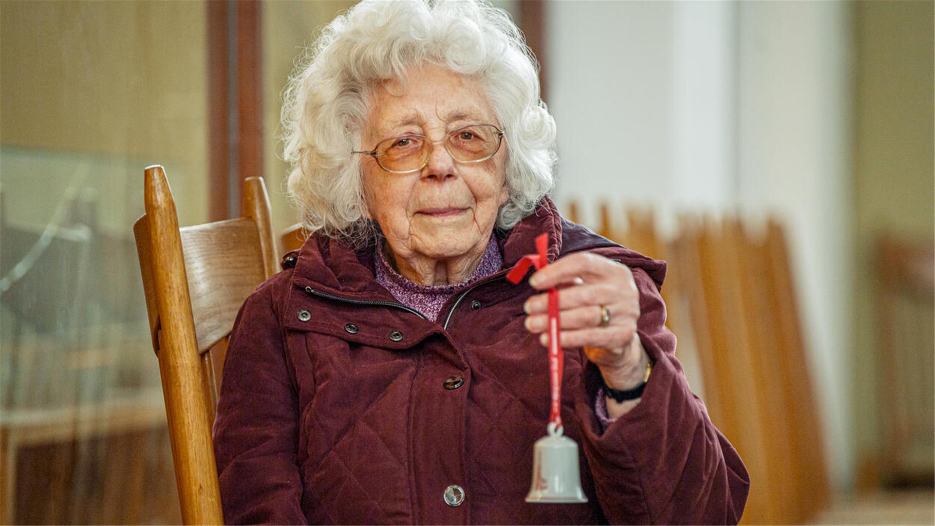 Eine Seniorin hält ein Glöckchen in der Hand.
