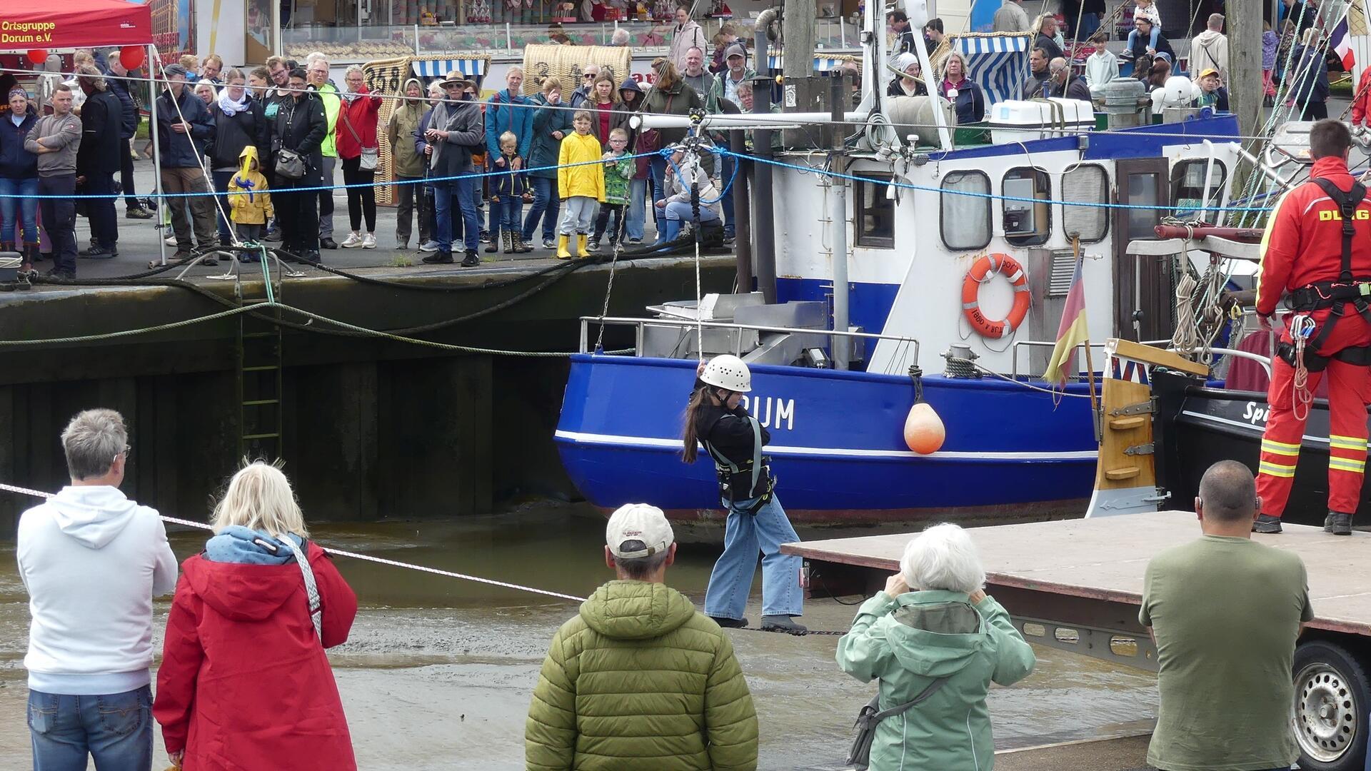 Viele Menschen in einem Hafen beobachten ein Mädchen auf einer Slackline über dem Hafenbecken.