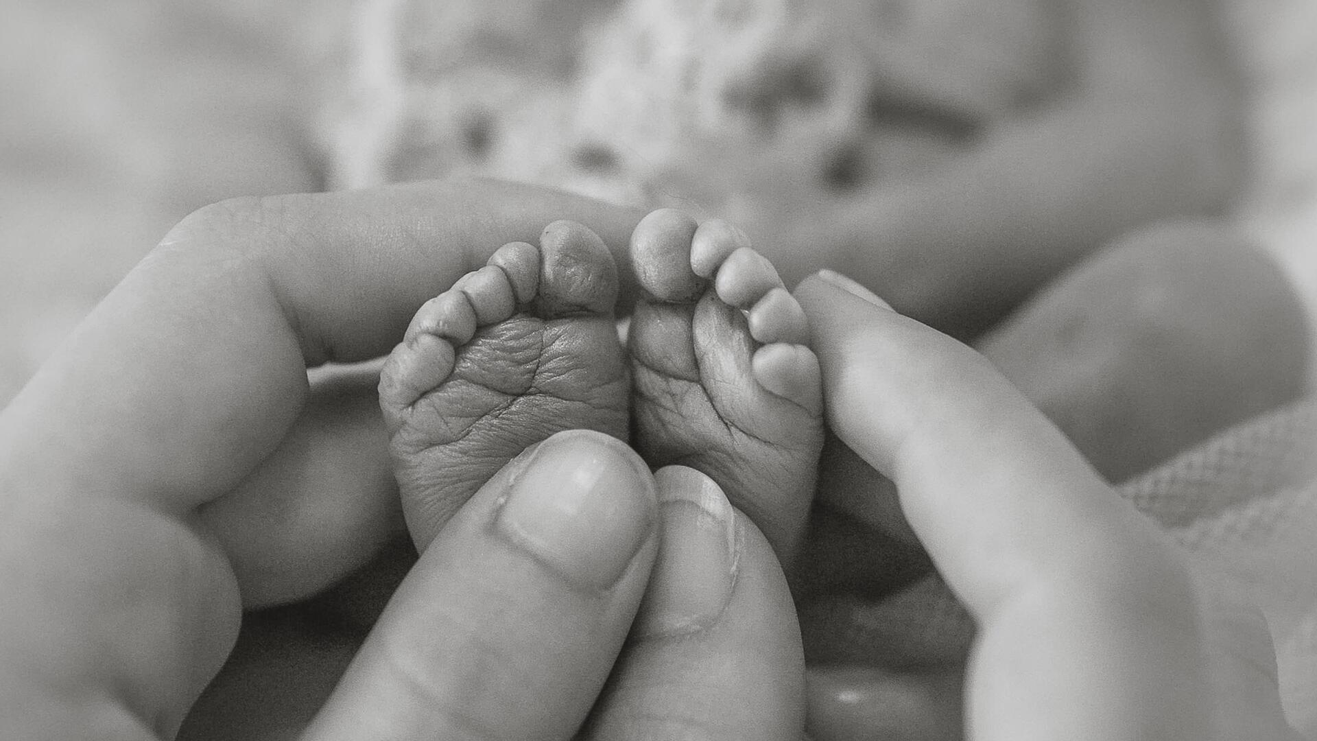 Zwei Hände halten zwei winzige Babyfüße.