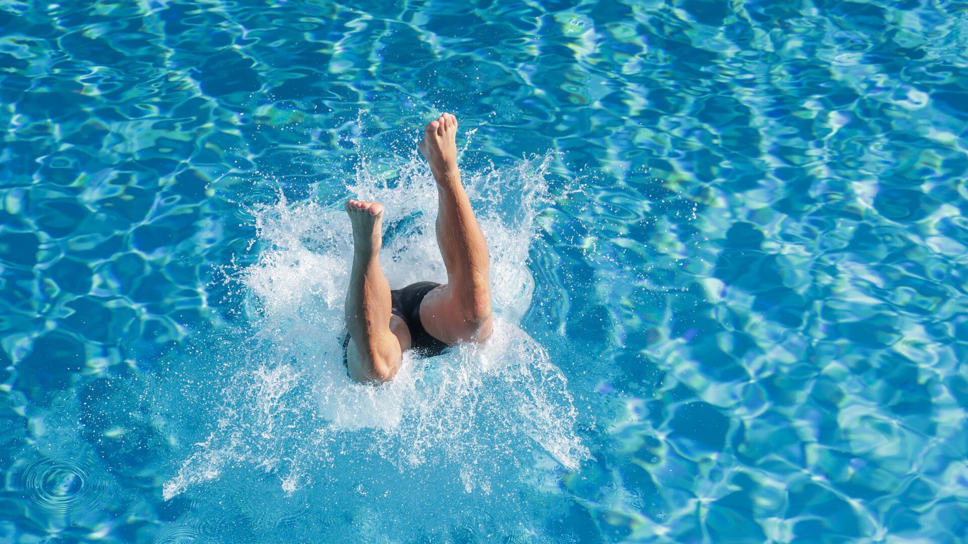 Ein Mensch springt in einem Freibad ins Wasser. Wenn es heiß wird, dann hilft unter anderem: ab ins Wasser!