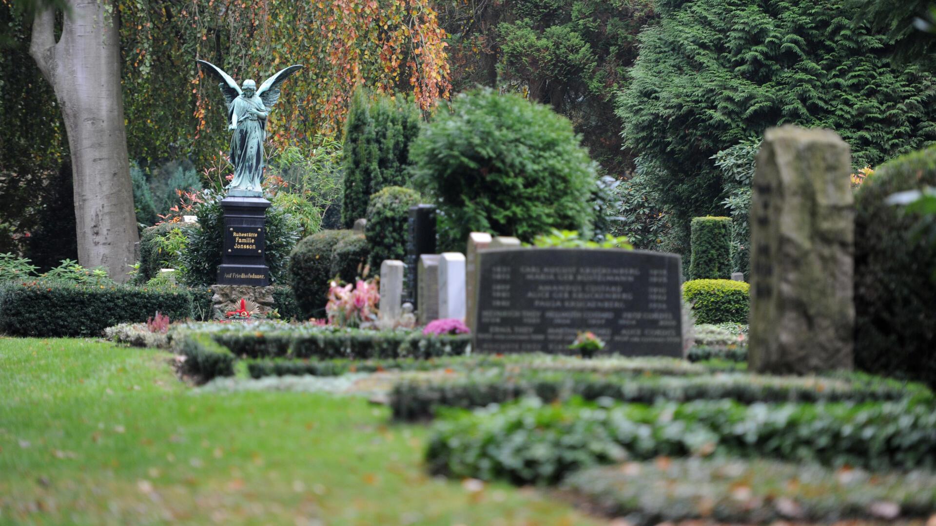 Ein Friedhof mit verschiedenen Grabsteinen und einer Engelstatue im Hintergrund. 