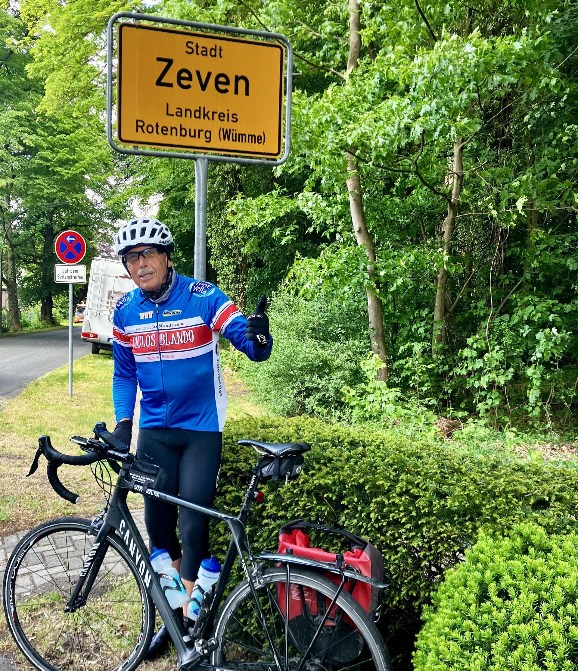Ein Mann mit einem Rennrad vor einem Ortsschild.