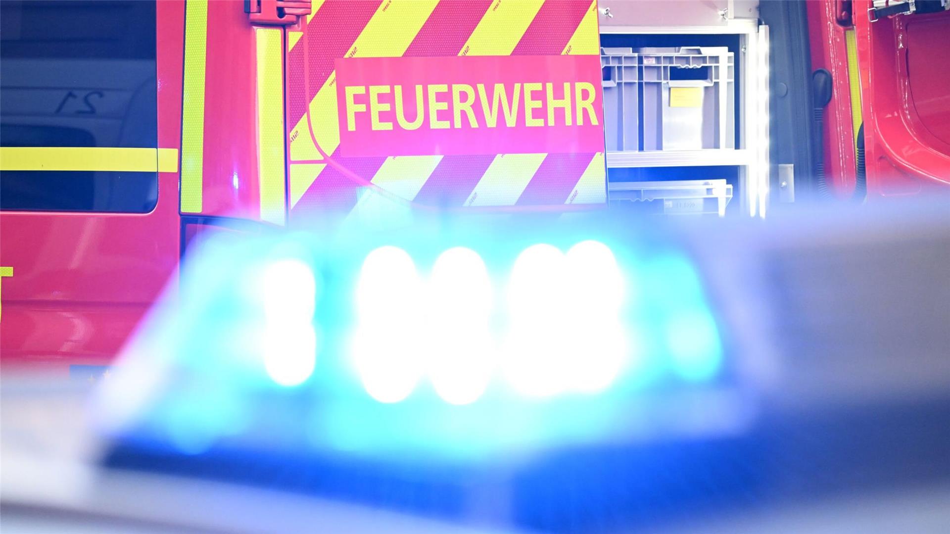 Ein Fahrzeug der Feuerwehr steht bei einem Einsatz auf einer Straße, während im Vordergrund das Blaulicht eines Polizeifahrzeugs zu sehen ist.