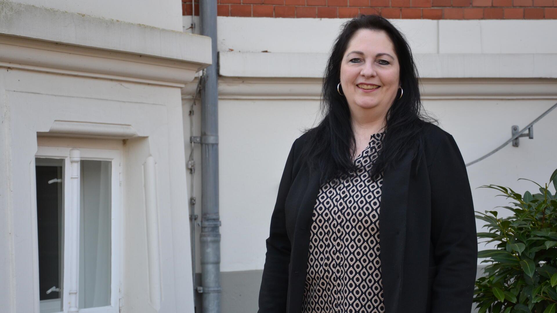 Christina Klinghagen, eine dunkelhaarige Frau, steht vor einer alten Stadtvilla in Zeven und lächelt in die Kamera.