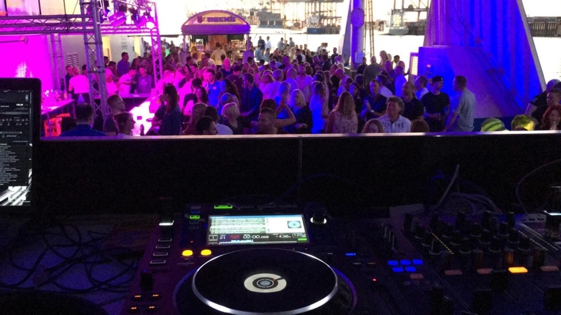 Feiernde Menschen und ein DJ-Pult auf einer Fähre, die vor Bremerhaven übers Wasser fährt.
