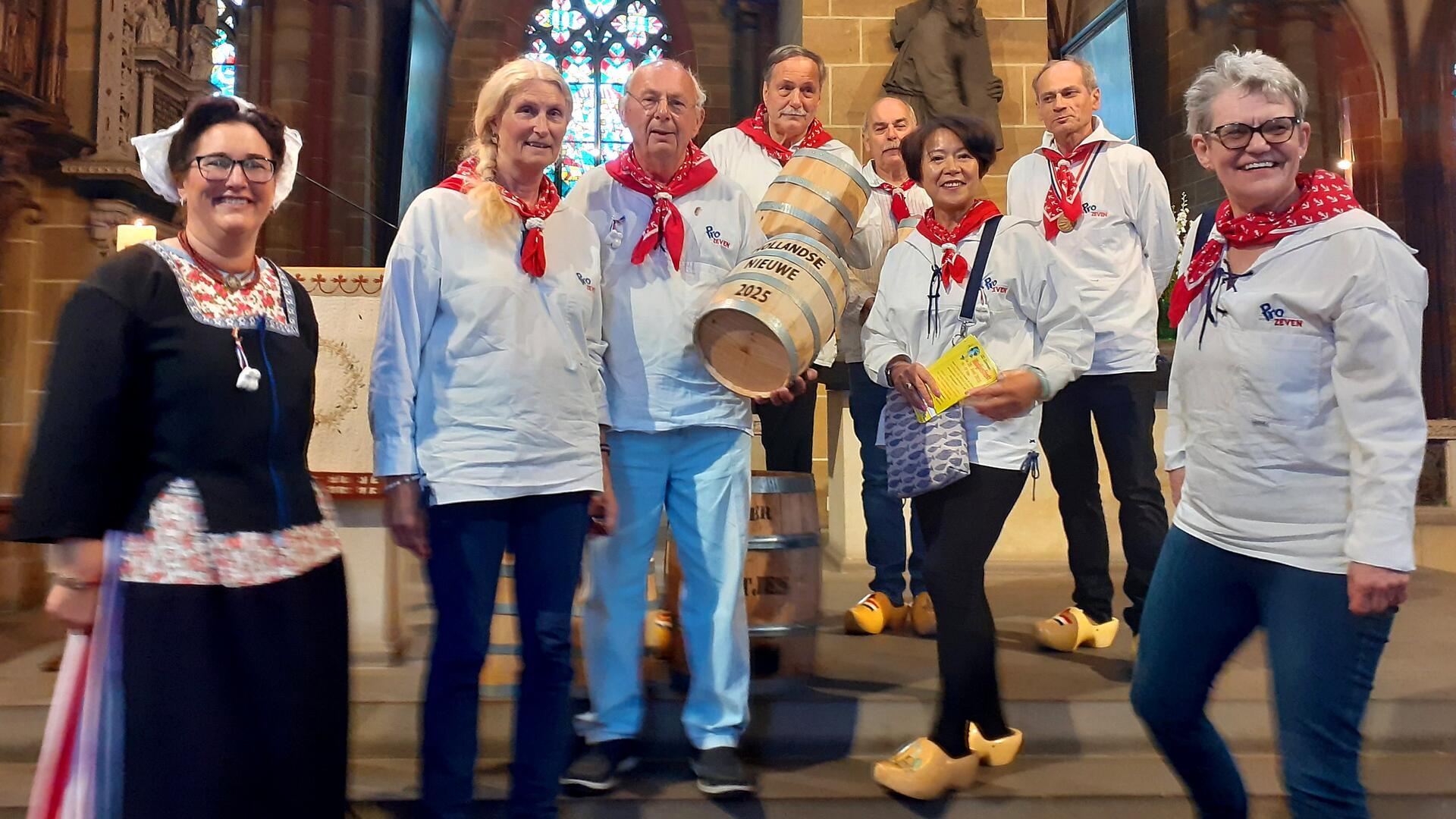Frauen und Männer in traditioneller Kleidung mit zwei Fässern lächeln in die Kamera.