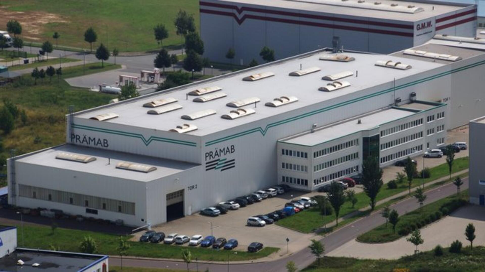 Luftaufnahme des Firmengebäudes der ehemaligen GMW PRÄMAB GmbH in Burg bei Magdeburg. Zu sehen sind die große Produktionshalle mit dem Schriftzug „PRÄMAB“ und ein angrenzendes Verwaltungsgebäude, umgeben von Parkplätzen und Grünflächen.