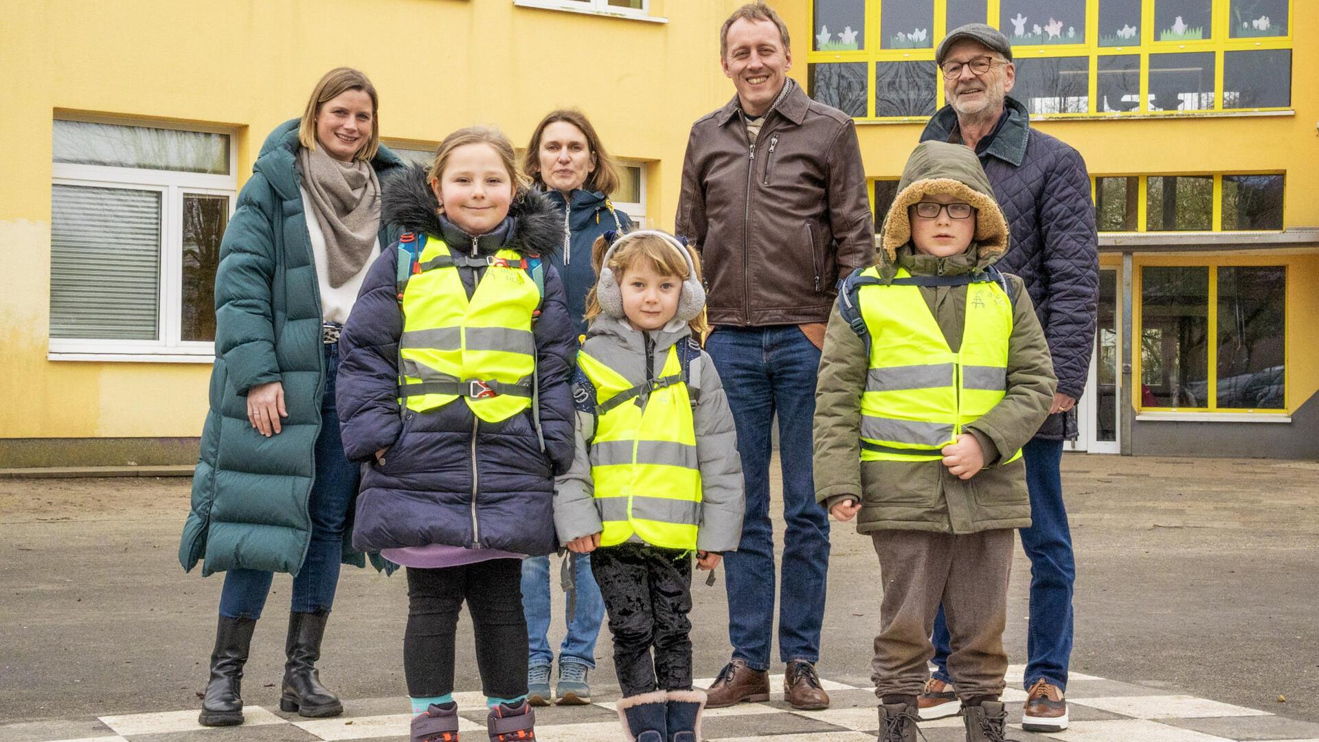 Gruppenfoto mit vier Erwachsenen und drei Kindern (die gelbe Warnwesten tragen) vor einer Schule. Projekt „Schulwegenetz“: Start an der Friedrich-Ebert-Schule zur Förderung sicherer und eigenständiger Schulwege für Schüler.