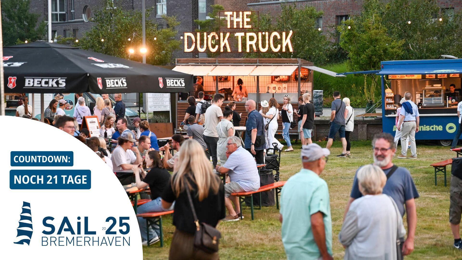 Viele Menschen schlendern über ein Streetfood-Festival auf einer Grünfläche.