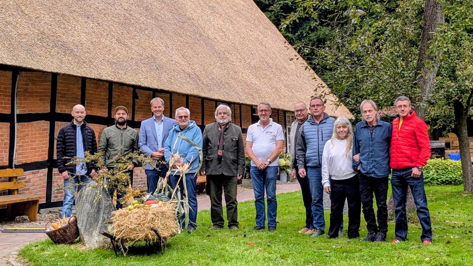 Gruppenbild vor dem Heimathaus Wachholz in Beverstedt mit frisch saniertem Reetdach. Mitglieder des Heimatvereins und Gäste stehen auf der Wiese vor dem Gebäude.