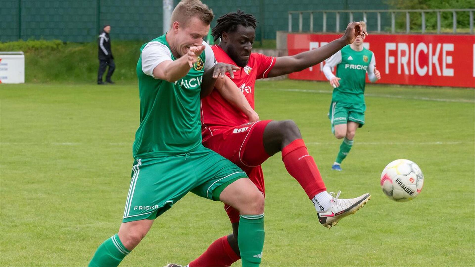 Zwei Männer in grünen und roten Trikots kämpfen um einen Ball.
