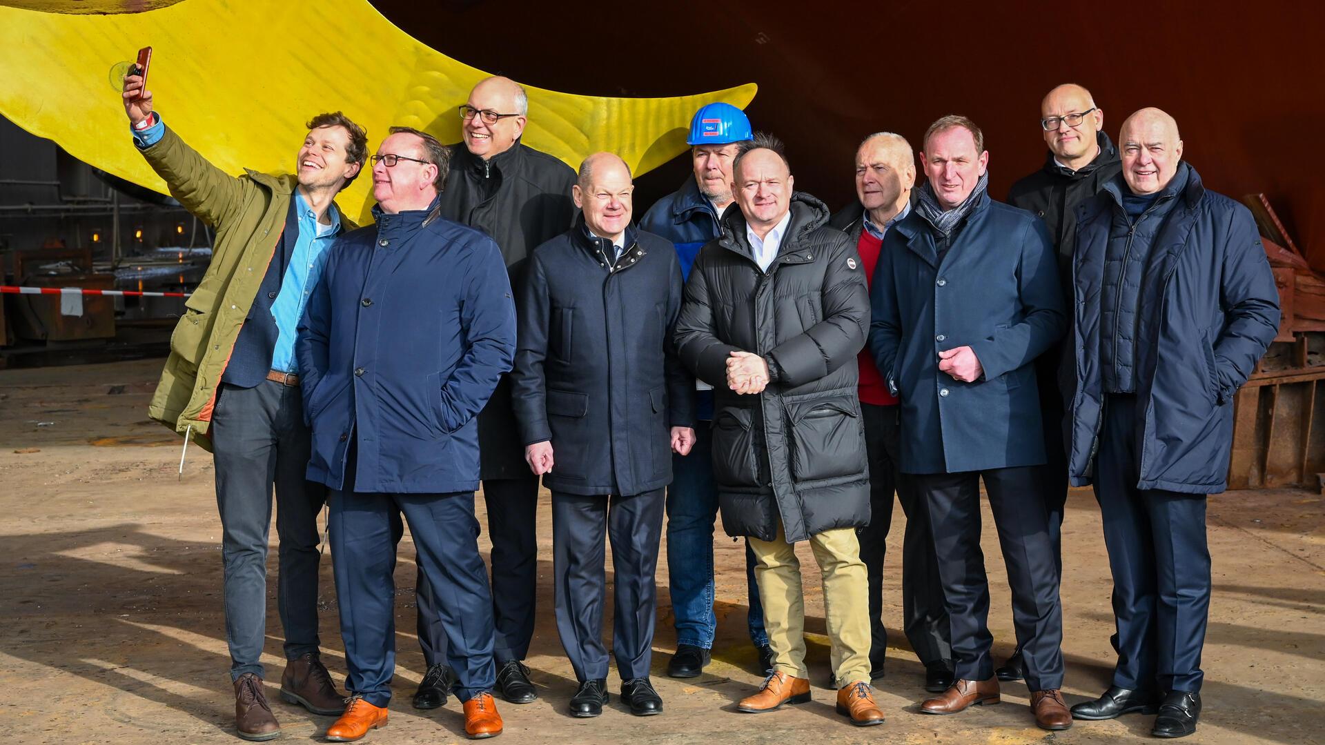 Zweigeteilt (v.l.): Falk Wagner (SPD Bremen), Bundestagsabgeordneter Uwe Schmidt und Bremens Regierungschef Andreas Bovenschulte lächeln fürs Selfie, während Kanzler Olaf Scholz mit den Gastgebern (v.l.) Betriebsrat Niels Bothen, Thorsten Rönner, Heinrich Rönner, Friedrich Norden, Heiner Rönner, Kurt Zech posiert.