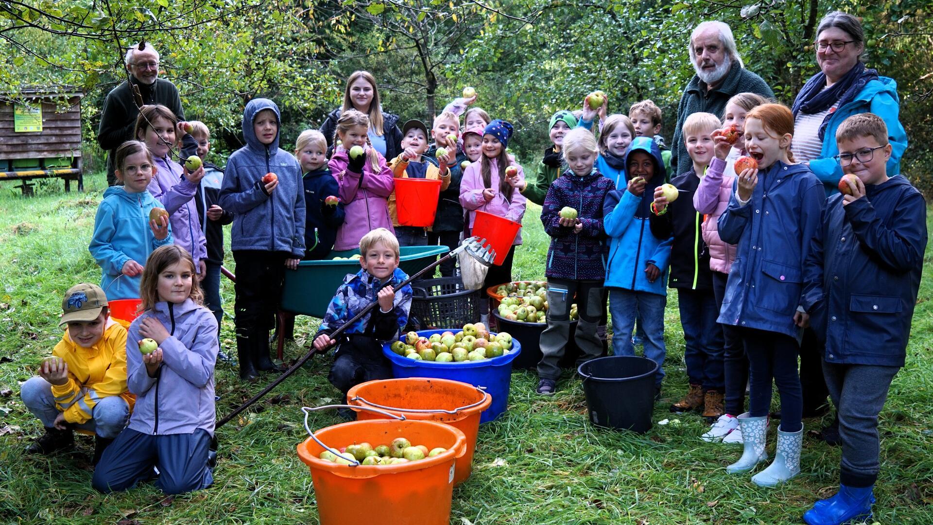 Kinder knien und stehen um Eimer herum, die mit Äpfeln gefüllt sind. 