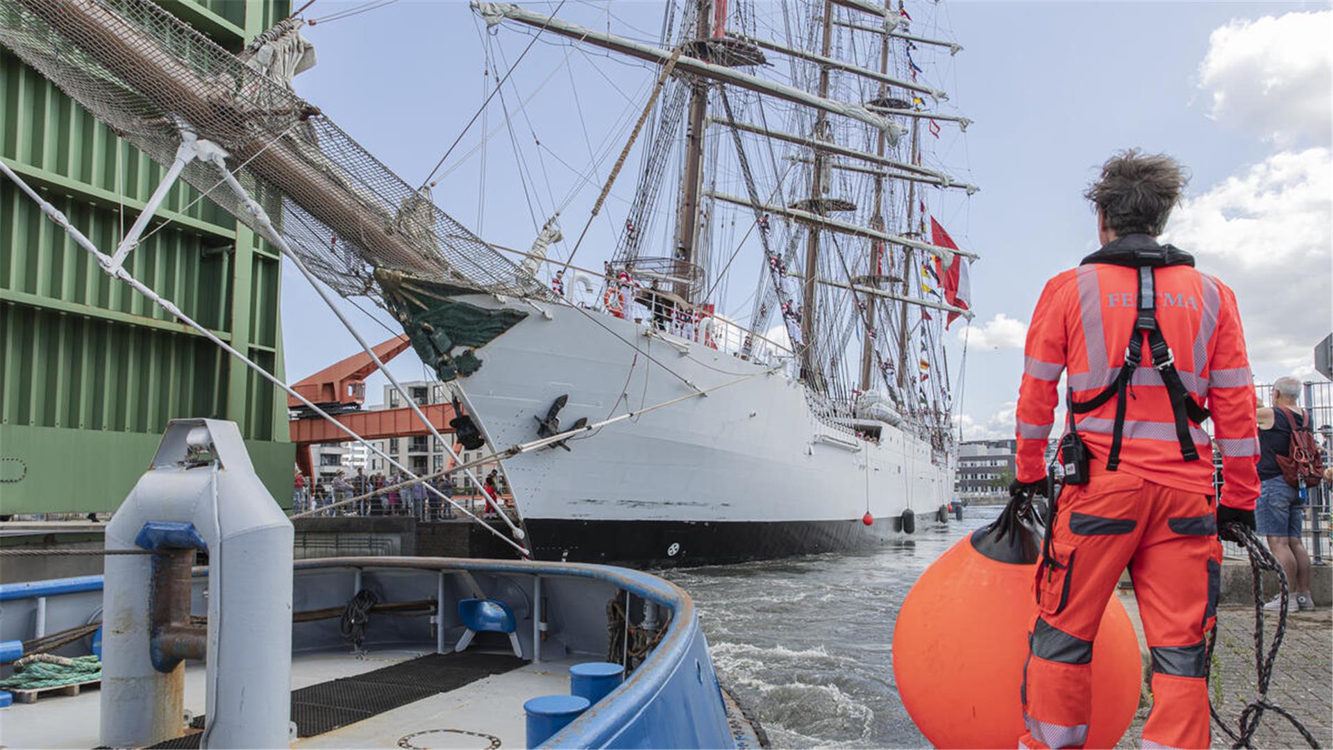 Ein Mann mit einem Fender, im Hintergrund ein großes Segelschiff.