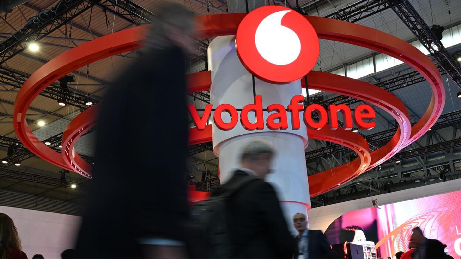 Menschen gehen an einem großen Vodafone-Aufsteller vorbei.